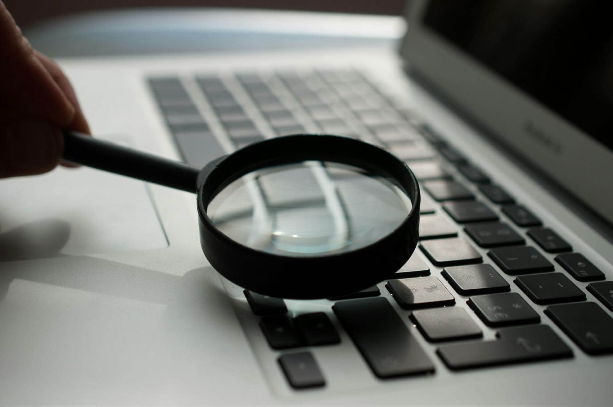 A magnifying glass over a laptop keyboard, symbolising how to identify click fraud.