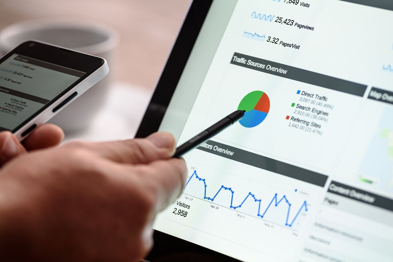 A man points a pen at a computer screen showcasing target audience traffic source data.